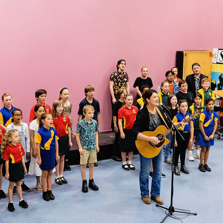 Group of school students singing with an adult playing the guitar