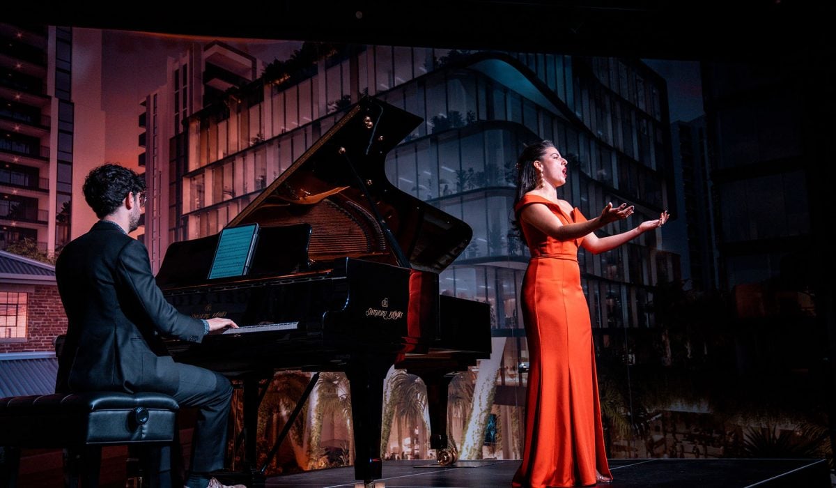 Opera singer dressed in red long dress and pianist playing on the background